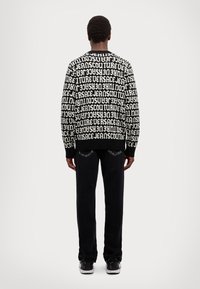 Maglione in bianco e nero con un motivo testuale ripetuto, abbinato a pantaloni scuri. Il maglione presenta un collo a giro e maniche lunghe, con polsini a costine.