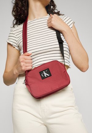 Borsa a tracolla Calvin Klein in tessuto rosso, forma rettangolare, con una patch logo nera, chiusura con zip e tracolla regolabile.
