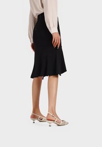 Gonna nera a campana con una texture liscia, abbinata a scarpe slingback beige con punta affilata e un motivo decorativo sulla tomaia.