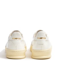 Sneaker in pelle bianca con suola in gomma beige e dettagli di cucitura. "LLOYD" in rilievo dorato sulla linguetta del tallone. Design classico.
