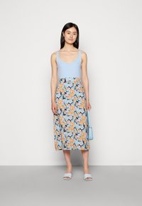 Top azul sem mangas com decote em V, combinado com uma saia midi de estampado floral com flores laranja e azuis sobre um fundo escuro.
