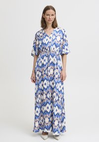 Robe maxi en bleu, blanc et pêche avec un motif géométrique. Comprend des manches courtes, une taille à cordon et un tissu fluide.