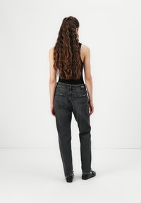 Jeans neri a vita alta con design a gamba dritta, dotati di tasche posteriori e leggera scoloritura. Indossati con un top nero senza maniche e scarpe basse.