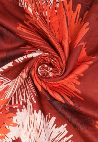 Sciarpa rossa e arancione con un motivo floreale vorticoso, realizzata in tessuto morbido, caratterizzata da diverse trame e colori che si fondono l'uno nell'altro.