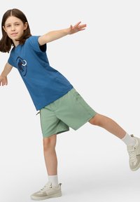 Blauwe katoenen T-shirt met een cirkelvormige zwarte olifantenafbeelding, gecombineerd met groene shorts en beige sneakers, met witte enkelsokken.