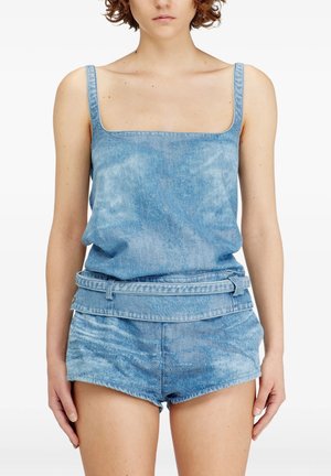 Donna che indossa un top smanicato in denim blu chiaro e pantaloncini in denim abbinati a vita alta con una cintura larga in vita.