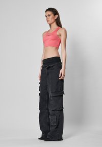 Rosa crop top og svarte cargo bukser, med flere lommer og løs passform. Glatt tekstur med kontrasterende farger og enkel design.