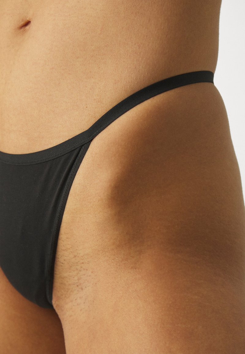 Zwarte zwemslips van gladde stof, met minimale bedekking en dunne elastische banden. Close-up weergave die de textuur benadrukt.