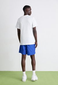 Vit bomull t-shirt, blå shorts och vita sneakers. Korta ärmar, avslappnad passform. Enkelt mönster utan synliga mönster eller detaljer.