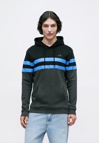 O hoodie preto apresenta riscas azuis horizontais, bolso canguru e capuz ajustável com cordão. Feito de um tecido macio e texturizado.