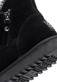 Bottine en daim noir avec fermeture éclair sur le côté, doublure en fourrure et semelle en caoutchouc texturée avec des rainures profondes pour une meilleure traction.