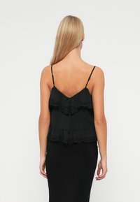 Débardeur noir à couches avec dentelle, doté de bretelles spaghetti ajustables et d'une fermeture à boutons au dos. Texture lisse et design fluide.