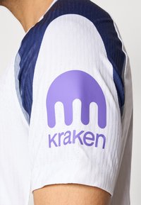 Hvid sportstrøje med struktureret stof, med marineblå detaljer på skuldrene og et lilla Kraken-logo på ærmet.