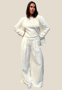 Hvit linjakke med vide bukser og skreddersydd jakke, kombinert med en tettsittende hvit topp. Glatt tekstur, minimalistisk design og rene linjer.