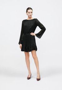 Zwarte geplooide jurk met lange mouwen, een gerimpelde zoom en een riem met een decoratieve ketting. Soepele textuur en een aansluitende silhouet.