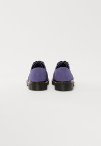 Pantofi din suede violet cu tălpi negre, având tocuri rotunde și șireturi asortate. Cusături notabile de culoare galbenă pe marginile tălpii.