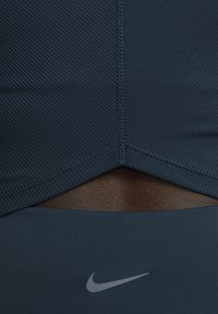 Top corto sportivo blu scuro con tessuto a coste testurizzato, dotato di un design elegante con taglio a spirale e un piccolo logo Nike argentato nella parte inferiore.