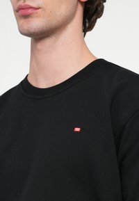 Čierna mikina z bavlny s okrúhlym výstrihom a rebrovanými manžetami. Na ľavej strane na hrudi má malú červeno-bielu logo.