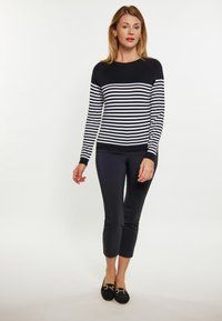 Schwarz-weißer gestreifter Pullover mit langen Ärmeln, rundem Halsausschnitt und taillierter Passform, kombiniert mit schwarzen verkürzten Hosen und schwarzen Slippern.