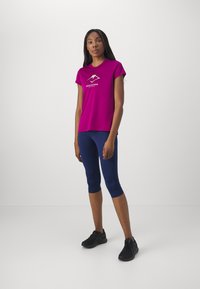 Camiseta deportiva fucsia de manga corta con gráfico de montaña, combinada con leggings capri azul marino, que presentan una tela suave y elástica.