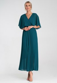 Turkusowa sukienka maxi z fasonem owijanym, z falbanistymi rękawami i plisowanym dołem. Wykonana z lekkiego materiału, z dekoltem w kształcie litery V i zwiewną teksturą.