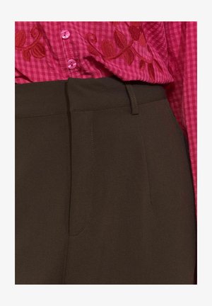 Rjave hlače z gladko teksturo, z stranskimi žepi in ozko silhueto. V kompletu s roza karirasto srajco, izvezeno z rdečimi listi.