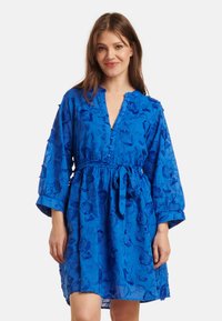 Blue embroidered dress with a tie waist, featuring three-quarter sleeves and floral patterns throughout. Made of lightweight fabric.