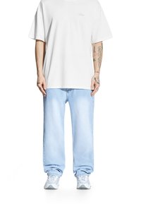 Biała koszulka z krótkim rękawem, luźny krój; jasnoniebieskie, szerokie dżinsy; w połączeniu z białymi trampkami z szarymi akcentami i teksturowaną podeszwą.