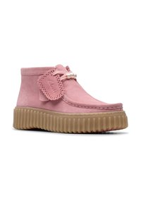 Botas de tobillo de ante rosa con punta redondeada, adornadas con lazo decorativo y detalle de perlas, y una suela de goma texturizada y estriada.