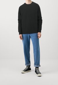 Felpa nera con collo girocollo, abbinata a jeans azzurri chiari e sneakers nere alta. Design semplice con una vestibilità rilassata.