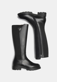 Bottes noires montantes en cuir lisse et textile. Détail de fermeture éclair sur le côté et semelle en caoutchouc texturé et épais.