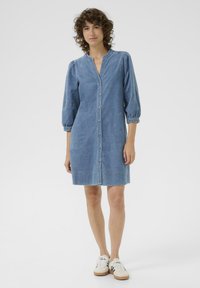 Denimmekko, jossa on nappikiinnitys, syvä V-aukko ja puffihihat. Vaalea sininen väri, polvipituinen, jossa on kaksi sivutaskua. Yhdistetty tennareiden kanssa.
