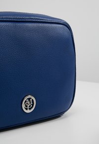 Borsa in pelle blu con superficie texturizzata, forma rettangolare e accento del logo argentato sul lato anteriore. Cuciture dettagliate lungo i bordi.