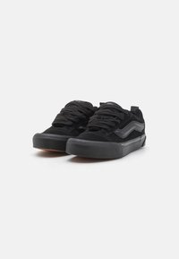 Baskets en daim noir avec des lacets plats, semelles en caoutchouc et liserés gris contrastants sur les côtés. Bout rond et détail de marque minimal sur la languette.
