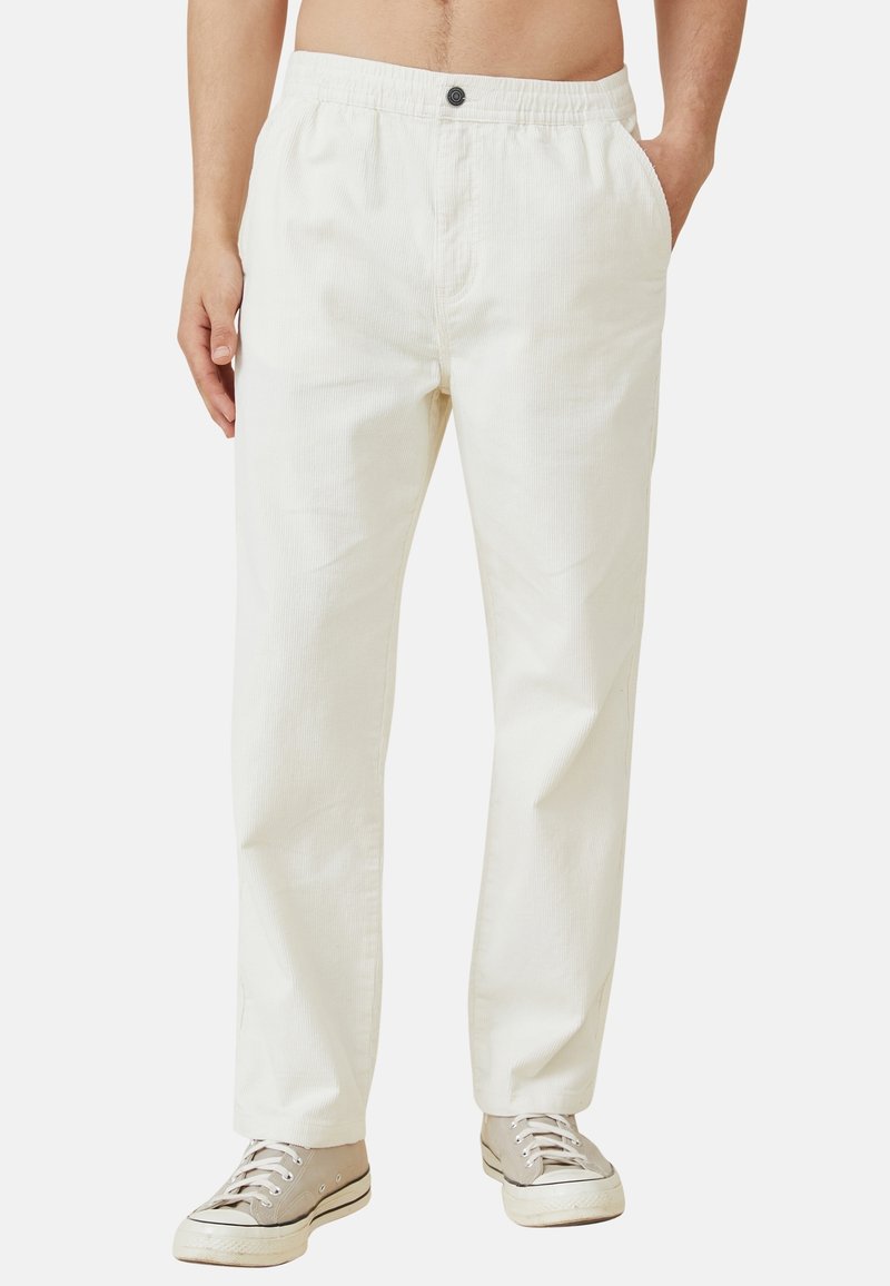 Witte katoenen broeken met een elastische tailleband en knoopsluiting. Rechte pijpen, gladde textuur, gedragen met beige sneakers.