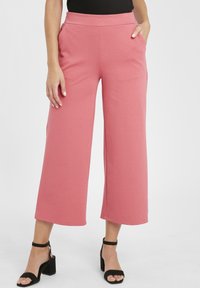 Rosa vidbyxade byxor av mjukt tyg, med hög midja och sidofickor. Matchas med svarta klacksandaler.