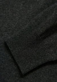 Dunkelgrauer gestrickter Pulloverstoff mit geripptem Bund. Das Material erscheint weich mit einer feinen Textur und zeigt eine Nahaufnahme des Webmusters.