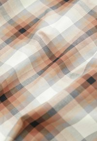 Tissu doux avec un motif à carreaux beige, blanc, gris et noir comprenant de petits carrés uniformément espacés et de légères rides.