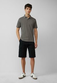 Polo gris à manches courtes, associé à un short cargo noir et des baskets blanches. Le polo a un col classique et une texture douce.