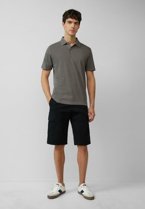 Polo gris à manches courtes, associé à un short cargo noir et des baskets blanches. Le polo a un col classique et une texture douce.