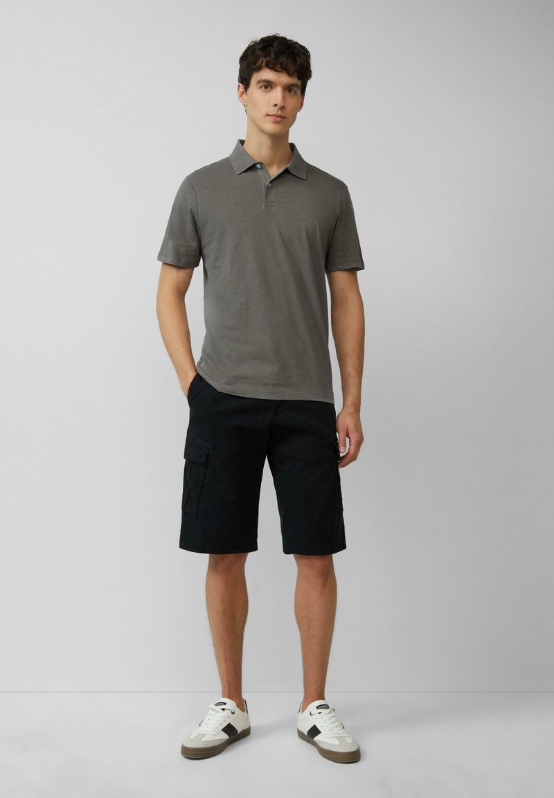 Polo gris à manches courtes, associé à un short cargo noir et des baskets blanches. Le polo a un col classique et une texture douce.