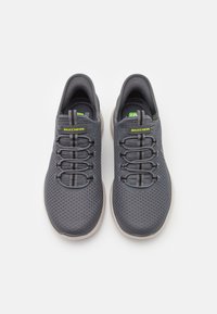 Gray athletic shoes with mesh upper and elastic lace system, featuring a cushioned sole and Skechers logo in yellow on the tongue.