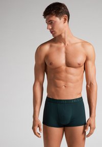 Tmavě zelené boxerky vyrobené z hladkého materiálu, s přiléhavým střihem a pružným pasem s decentním logem.