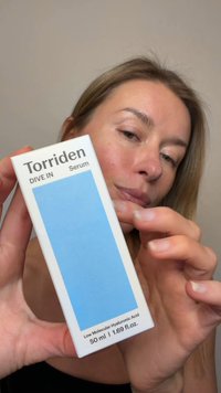 Donna che tiene una scatola del siero Torriden Dive In con etichetta blu, che evidenzia l'acido ialuronico a basso peso molecolare, formato da 50 ml.