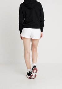 Sudadera negra con un bolsillo frontal tipo canguro, combinada con pantalones cortos blancos y zapatillas negras. Cuenta con capucha ajustable y puños acanalados.