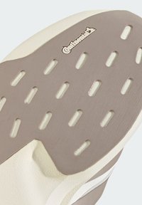 Εξωτερική σόλα παπουτσιού με μπεζ λαστιχένιο πέλμα που διαθέτει οριζόντιες σχισμές και ανάγλυφο λογότυπο Continental κοντά στο επάνω μέρος.