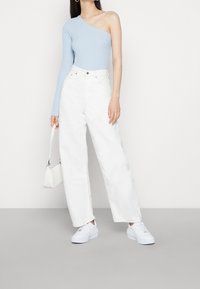 Světle modrý top na jedno rameno z ribového materiálu, zkombinovaný s bílými kalhotami s vysokým pasem a širokými nohavicemi, a bílými platformovými teniskami, doplněný malou bílou taškou.