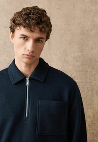 Námořnický fleece pulovr na poloviční zip s špičatým límcem a náprsní kapsou, se strukturovanou tkaninou a stříbrnými prvky na zipu.