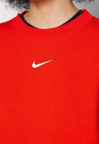 Roter Sweatshirt aus weichem Stoff mit Rundhalsausschnitt und kleinem weißen Nike-Logo auf der Brust. Strukturierter, lässiger Stil.