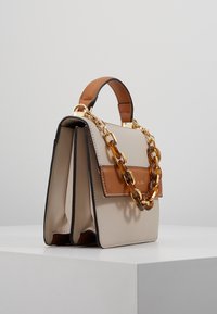 Bolso de mano de cuero beige con detalles en marrón, doble compartimento, herrajes dorados y una correa de cadena gruesa. Textura suave con costuras en contraste.